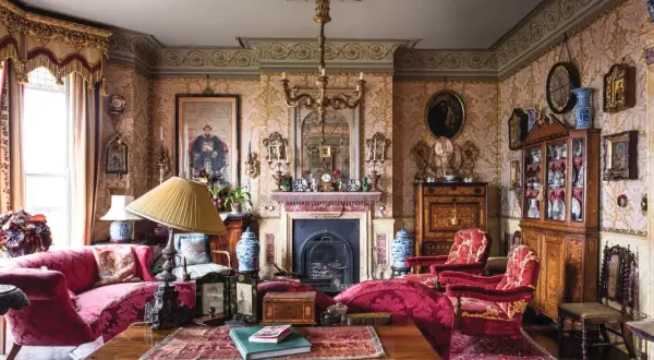 A lavish Victorian interior design with ornate wallpaper, plush red furniture, a fireplace, and antique decor.
