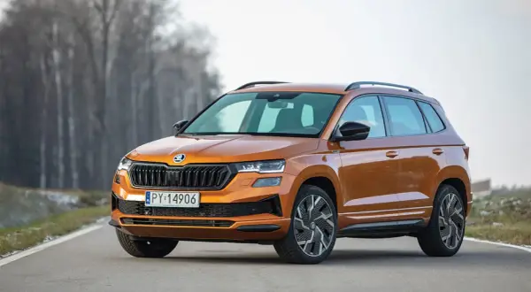 Pomarańczowy Skoda Karoq Sportline na drodze, z drzewami w tle.