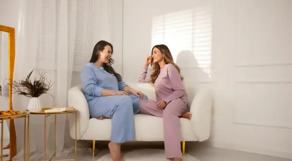 Dwie kobiety w pastelowych piżamach plus size rozmawiają na kanapie.