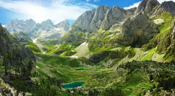 Magnifique paysage de montagne pour un trek en Albanie, avec des lacs d'un bleu profond et des pentes verdoyantes sous un ciel ensoleillé.