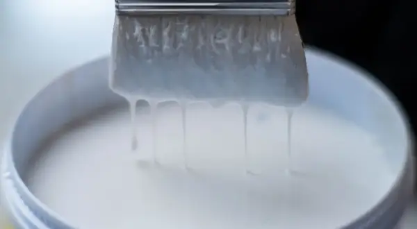 Pennello intriso di vernici all'acqua, gocciolanti in un secchio bianco.