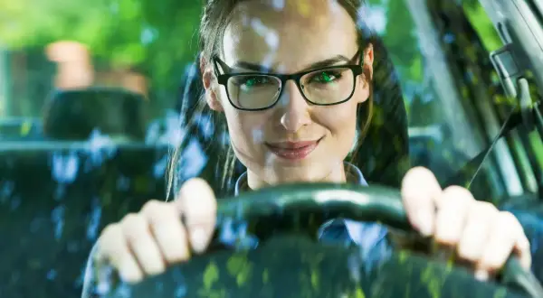Frau mit Brille am Steuer, bereit zum Autofahren.