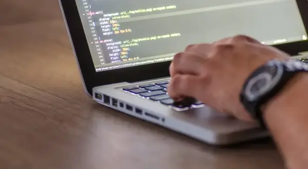 Dłoń programisty pisze kod na laptopie. Zastanawiasz się, ile zarabia programista po studiach?