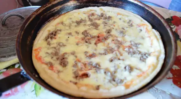 Pizza à la poêle, garnie de viande hachée et de fromage fondant, prête à être dégustée.