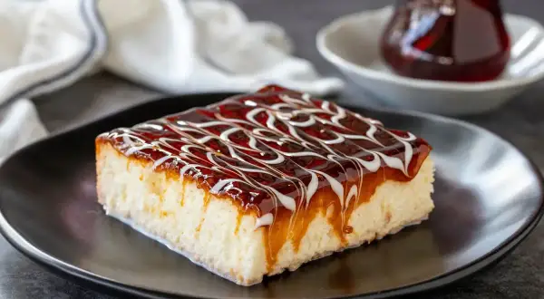 Una fetta di torta trilece ricetta, bagnata da sciroppo e caramello, su piatto nero.