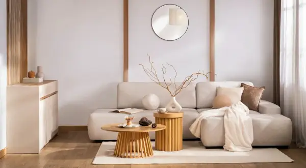 Salon w stylu zen. Jasna kanapa, drewniane stoliki, okrągłe lustro i subtelne dekoracje tworzą oazę spokoju.