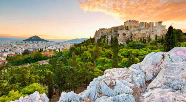 Akropolis reser sig över Aten, greklands huvudstad, med en dramatisk solnedgång i bakgrunden.