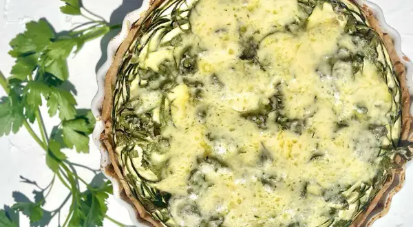 Eine köstliche Zucchini-Quiche mit goldbraunem Teig und einer cremigen Füllung, garniert mit frischer Petersilie.