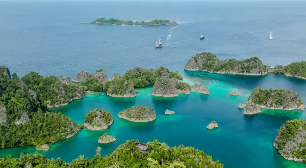 Traumhafte Anreise nach Raja Ampat: türkisfarbene Lagunen, grüne Inseln und Segelschiffe im azurblauen Meer.