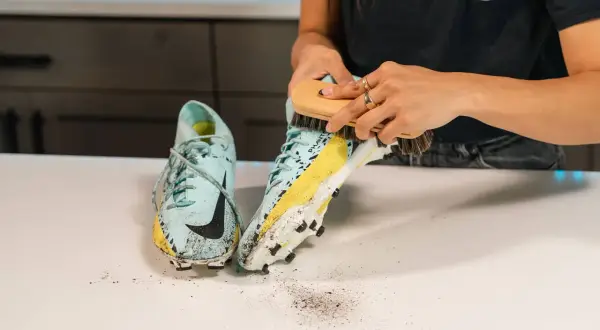 Mani che spazzolano scarpe da calcio sporche di fango, un passo fondamentale per capire come lavare le scarpe da calcio e mantenerle in forma.