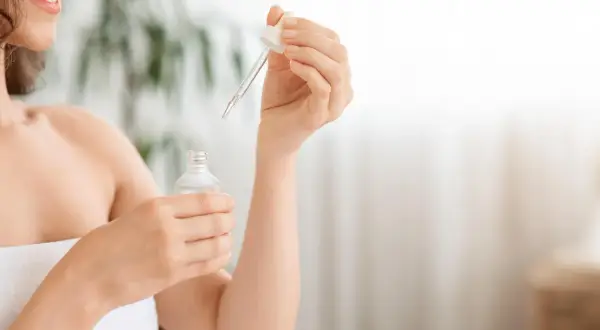 Kobieta z uśmiechem na twarzy aplikuje serum z niacynamidem i witaminą C na skórę.