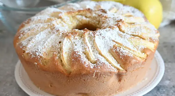 Ciambella alle mele soffice e profumata, cosparsa di zucchero a velo, con mele a vista.