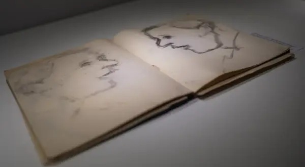 Szkice portretowe w otwartym szkicowniku. Po prawej stronie profil mężczyzny, po lewej ledwo widoczny zarys twarzy. Dzieło Artura Nachta Samborskiego.