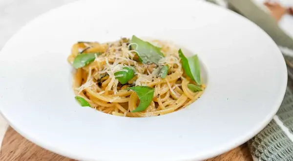 En portion spaghetti alla nerano, krämig och toppad med färsk basilika och riven ost.