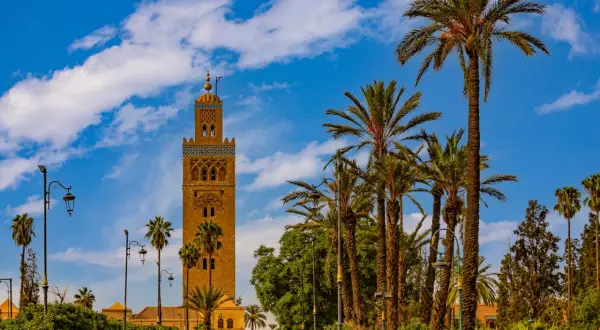 Torre Koutoubia, un lugar que ver en Marrakech, rodeada de palmeras y bajo un cielo azul con nubes.