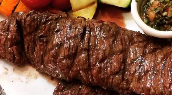 Jugosa entraña de vaca a la parrilla, acompañada de verduras asadas y una salsa chimichurri.