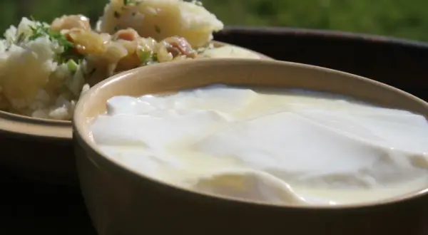 Gęste, białe zsiadłe mleko w glinianej miseczce, obok ziemniaków z koperkiem. Prosty przepis, jak zrobić zsiadłe mleko.