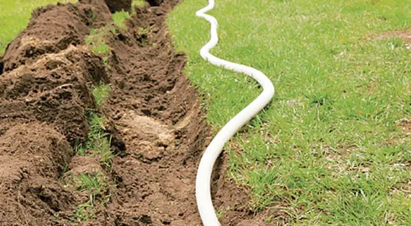 Ein Graben wird für das Erdkabel verlegen vorbereitet. Ein weißes Kabel schlängelt sich über das Gras neben dem aufgeworfenen Erdreich.