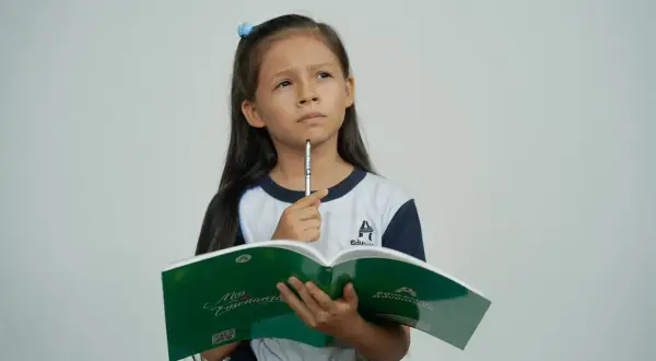 Bambina pensierosa con libro aperto, cerca la risposta a indovinelli per bambini.
