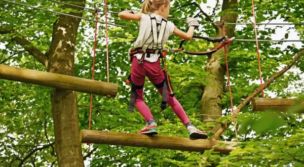 Ein Mädchen balanciert auf einem Baumstamm in einem Kletterpark. Ein spannendes Abenteuer für die **Herbstferien 2026**!