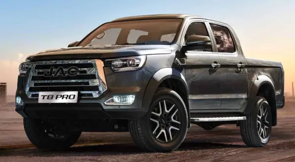 Ciemnoszary pickup JAC T8 PRO z chromowanym grillem i felgami stoi na piaszczystym podłożu.