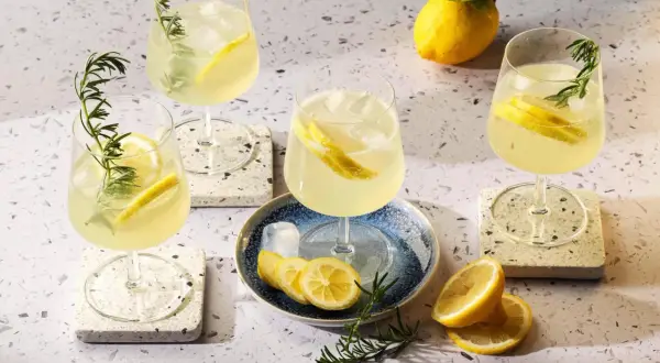 Quattro bicchieri di rinfrescante limoncello spritz, guarniti con limone e rosmarino, su un tavolo luminoso.