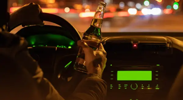 Kierowca trzyma butelkę piwa za kierownicą w nocy. W Niemczech obowiązuje ścisły limit alkoholu dla kierowców.