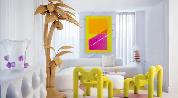 Sala de estar con vibrante arte abstracto, muebles curvos y un árbol de mimbre, todo con un audaz estilo Memphis.