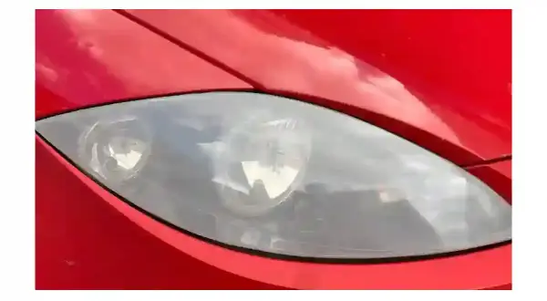 Gros plan sur un phare opaque de voiture rouge, reflétant le ciel.