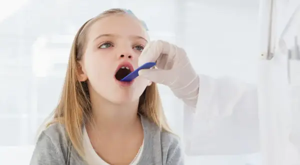 Niña con la boca abierta, examinada por un médico. Podría ser una consulta previa a una **operación amígdalas niños**.