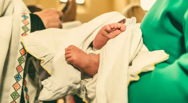 Les petits pieds d'un bébé, enveloppés dans un linge blanc orné, lors d'un baptême catholique.