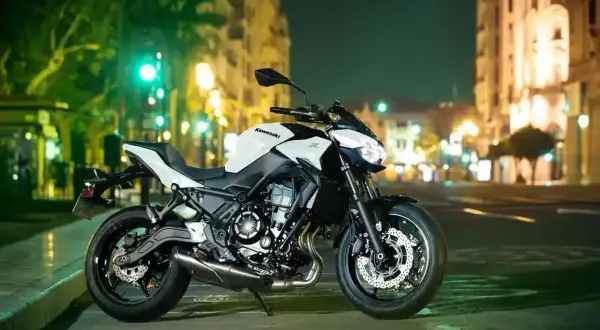 Kawasaki z650 cv blanca y negra, aparcada en una calle urbana de noche, con luces de edificios y semáforos de fondo.