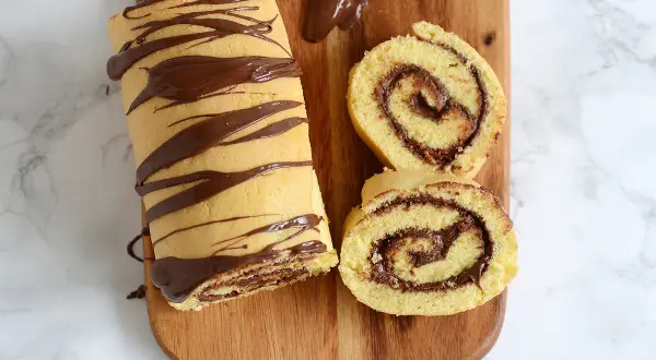 Un roulé au Nutella, entier et tranché, décoré de chocolat fondu sur une planche en bois. Un délice gourmand !