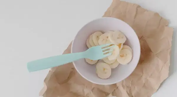 Miseczka z plasterkami banana i niebieskim widelcem. Czy królik może jeść banana? To pytanie nurtuje wielu właścicieli tych uroczych zwierząt.