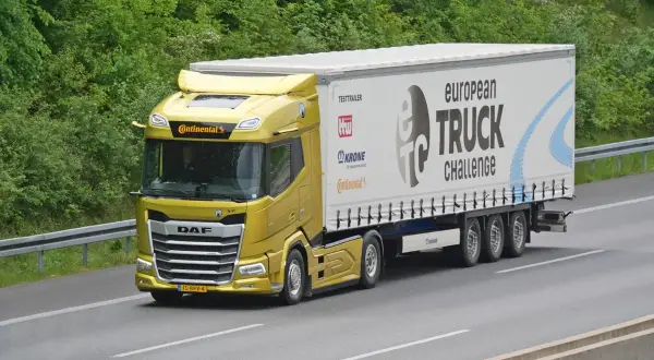Un camion jaune DAF XF participe au European Truck Challenge, sur une autoroute bordée d'arbres.