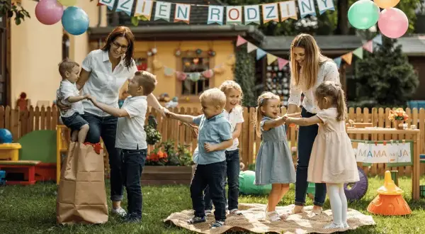 Radosne gry i zabawy dla dzieci klas 1-3 na przyjęciu urodzinowym w ogrodzie. Dzieci tańczą w kółku z opiekunkami, balony i girlandy tworzą świąteczną atmosferę.