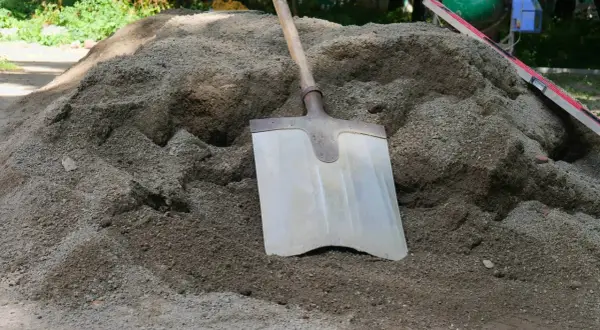 Łopata wbita w kopiec suchego betonu, obok poziomica.