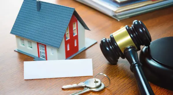 Modellino di casa, chiavi, martelletto da giudice e documenti su un tavolo di legno, evocano aste immobiliari tra privati.