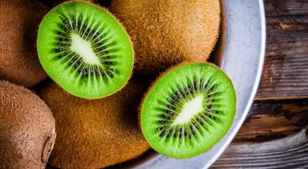 Kiwifruit w misce, przekrojone na pół, ukazujące zielony miąższ z czarnymi pestkami.