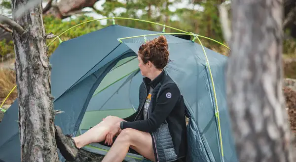 Kvinna vilar vid sitt tält, redo för camping i naturen.