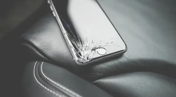 Uszkodzony ekran telefonu leżący na skórzanym siedzeniu.