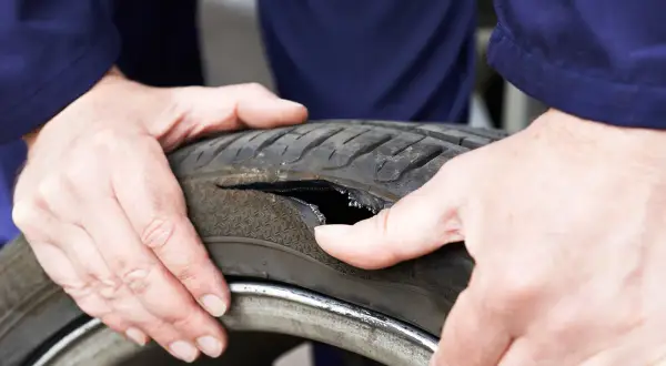 Dłonie mechanika pokazują oponę z dużym pęknięciem z boku. Widać wewnętrzną strukturę opony.
