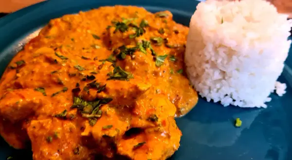 Ein Teller mit cremigem Hähnchen Tikka Masala, garniert mit frischer Petersilie, daneben ein Berg aus duftendem Reis.