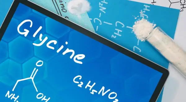 Tablet z napisem "Glycine" i wzorem chemicznym. Obok proszek w probówce. Dowiedz się, glicyna co to za związek.