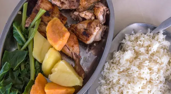 Sabrosa comida de Gambia: pollo asado, batatas, patatas y verduras verdes, acompañado de arroz blanco.