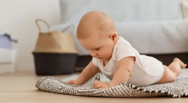 Dziecko na brzuchu, ćwiczy **wysoki podpór kiedy** na dywaniku.