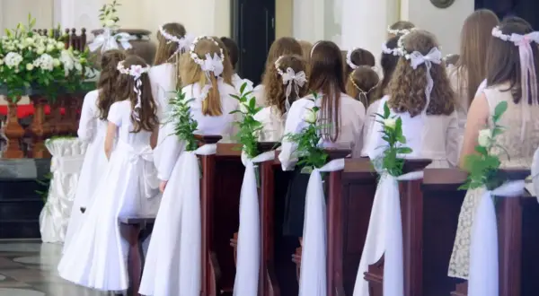 Dzieci w białych strojach, ozdobione wiankami, czekają na komunię. Zazwyczaj do komunii idzie się w wieku około 8-9 lat.