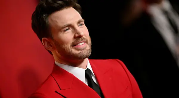 Chris Evans w czerwonym garniturze, jak z najlepszych filmów. Uśmiechnięty, z zarostem, prezentuje się elegancko.