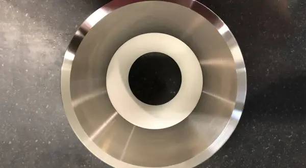 Componente metallico con finitura lucida, probabilmente acciaio inossidabile che contiene nichel, con un inserto bianco al centro.