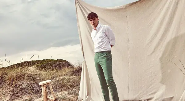 Uomo con camicia bianca e abbinamento pantalone verde su sfondo naturale.